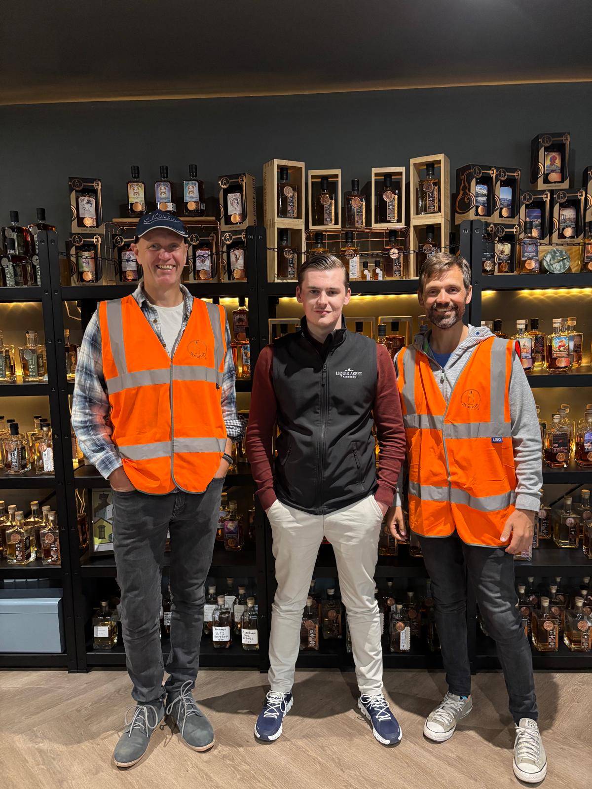 The Liquid Asset Partners team on a distillery visit, in front of shelves of single-cask bottled whisky
